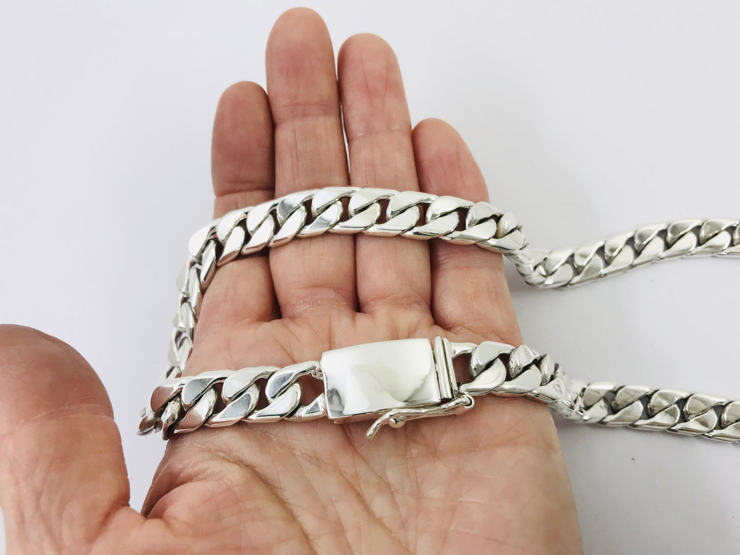 Silver chain necklace held in a hand against a white background